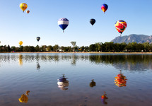 Hot air balloons  in the sky reflecting in the lake below.