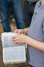 a teen boy reading from a Bible to a group 
