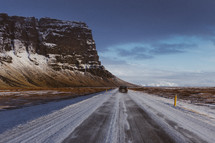 cliff with snow and a vehicle on a road 