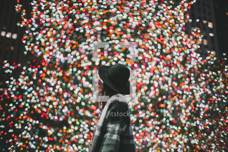 a woman looking at Christmas lights on a Christmas tree 