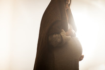 pregnant Mary holding her belly standing in glowing light 