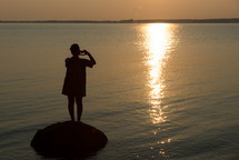 silhouette of a woman standing on a rock in a lake 