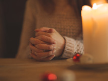 a woman with praying hands over a table by a candle at Christmas 