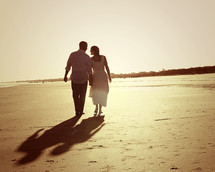 couple holding hands walking on a beach 