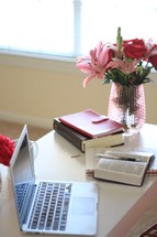 laptop computer, vase of flowers, notebook, and Bible on a desk 