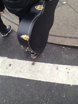 A guitar case being carried across a street.