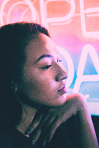 face of a young woman in front of a neon open sign 