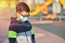 Disappointed lonely kid wearing mask for protection of corona virus spread on a closed empty park