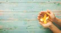 cupped hands holding a yellow ribbon 