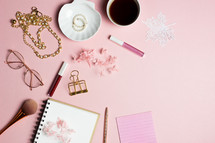 coffee cup, notebook, and makeup on a pink background 