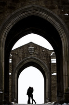 A couple embraces under archways of a building.