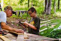 grandfather helping his grandson hammer nails into wood boards 
