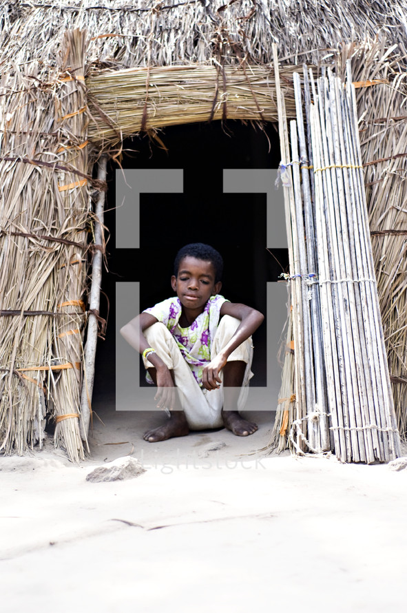 child in the entrance of a thatched hut