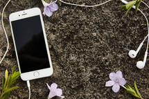 Smartphone with earbuds on a rock with flowers.
