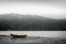 A small boat on a lake surrounded by trees and mountains.