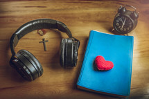 headphones, Bible, alarm clock, and red felt heart on a wooden table 