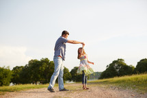 a father dancing with his daughter on a dirt road 