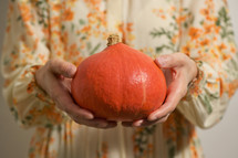 a woman holding an orange pumpkin 