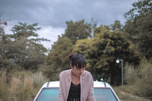 a young woman sitting on the hood of a car 