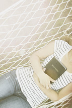 woman resting in a hammock holding a Bible 
