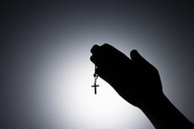 Silhouette photo - praying hands holding a rosary