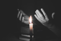 Black and white image of candlelight and a woman praying with open hands on a Bible 