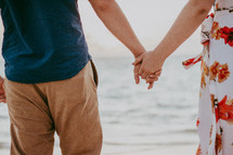 a couple holding hands walking on a beach 