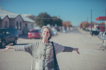 a woman standing in a street with outstretched arms 