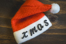 A little Santa hat with the letters Xmas on it. On a wooden background. background for Christmas.