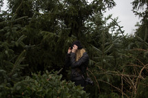 A woman pulling her hat down in a stand of trees and undergrowth.