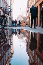 reflection in a puddle and people walking on a narrow street 
