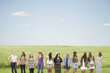 group of young women, standing in a line holding hands, in a field
