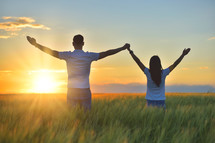 Young couple feeling free in a beautiful natural setting, in what field at sunset