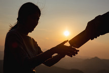Silhouette of a man giving a Bible to a woman at sunrise.