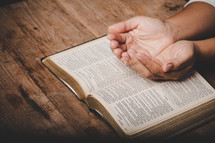 Woman praying with hands open on top of her open Bible