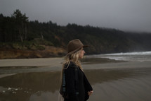 A young woman in a hat staring out at the ocean.