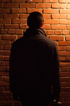 man with his back to the camera facing a brick wall 