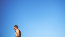 shirtless man against a blue sky backdrop 