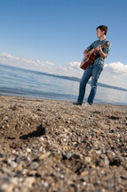 man playing a guitar in front of a lake