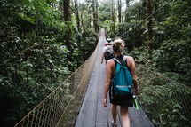 people crossing a swinging bridge in a jungle 