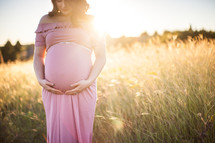 pregnant woman holding her belly standing in a field at sunset 