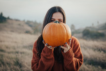 a woman holding up an orange pumpkin 