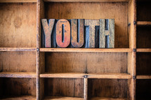 Wooden letters spelling "youth" on a wooden bookshelf.