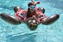 A little girl with goggles on a sea turtle pool float 