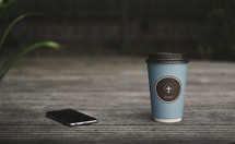 coffee cup with a cross on it and an iPhone 