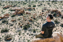 man sitting on a rock looking out at a desert landscape 
