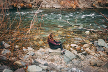 woman sitting on rocks along a riverbank 