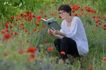 a woman reading a book sitting in a field of wildflowers 