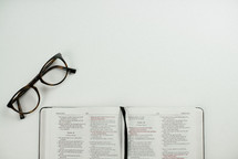 reading glasses and open Bible on a white desk 
