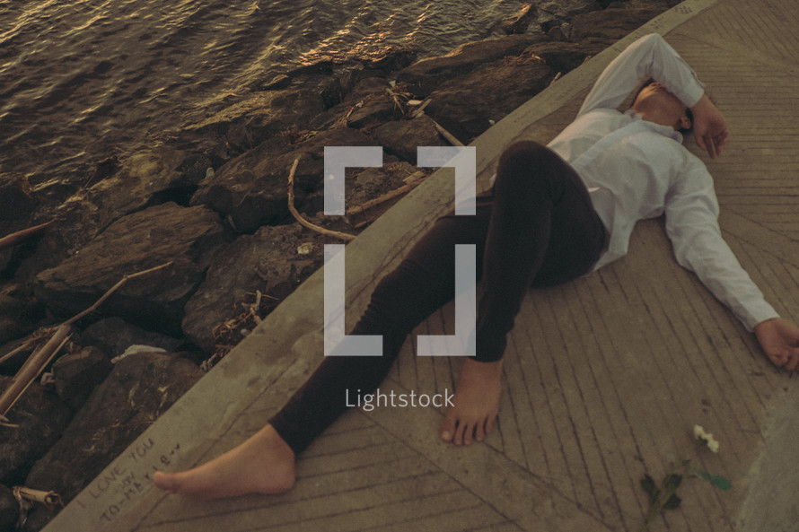 an exhausted man lying on a boardwalk beside a shore 